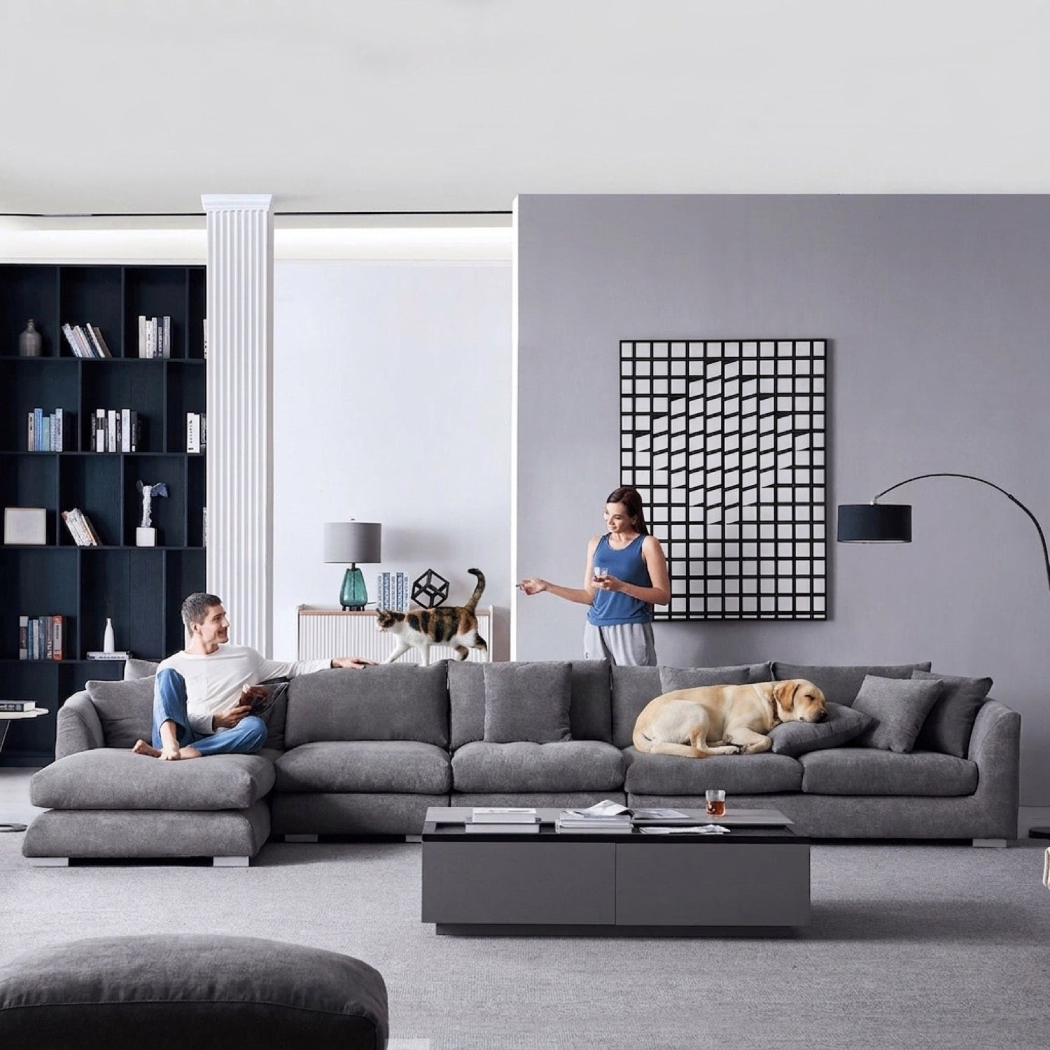 Grey sectional sofa in a modern living room with a man reading, a woman holding a drink, a cat, and a dog